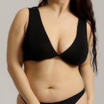 Woman wearing a black twist system and thong against a plain background
