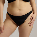 A woman wearing black thong underwear designed with a mid-rise cut.