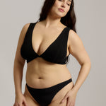 Woman wearing a black twist system and thong against a plain background