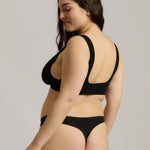 Woman wearing a black twist system and thong against a plain background