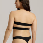 Woman wearing black strapless system against a neutral background