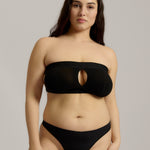 Woman wearing black strapless system against a neutral background