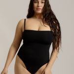 Woman wearing a black bodysuit against a plain background