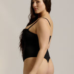 Woman wearing a black bodysuit against a plain background