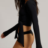 Woman wearing a black wrap top and black thong on a plain background
