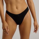 A woman wearing black thong underwear designed with a mid-rise cut.