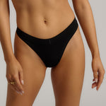 A woman wearing black thong underwear designed with a mid-rise cut.