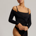 Woman wearing a black wrap top and black thong on a plain background