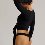 Woman wearing a black wrap top and black thong on a plain background