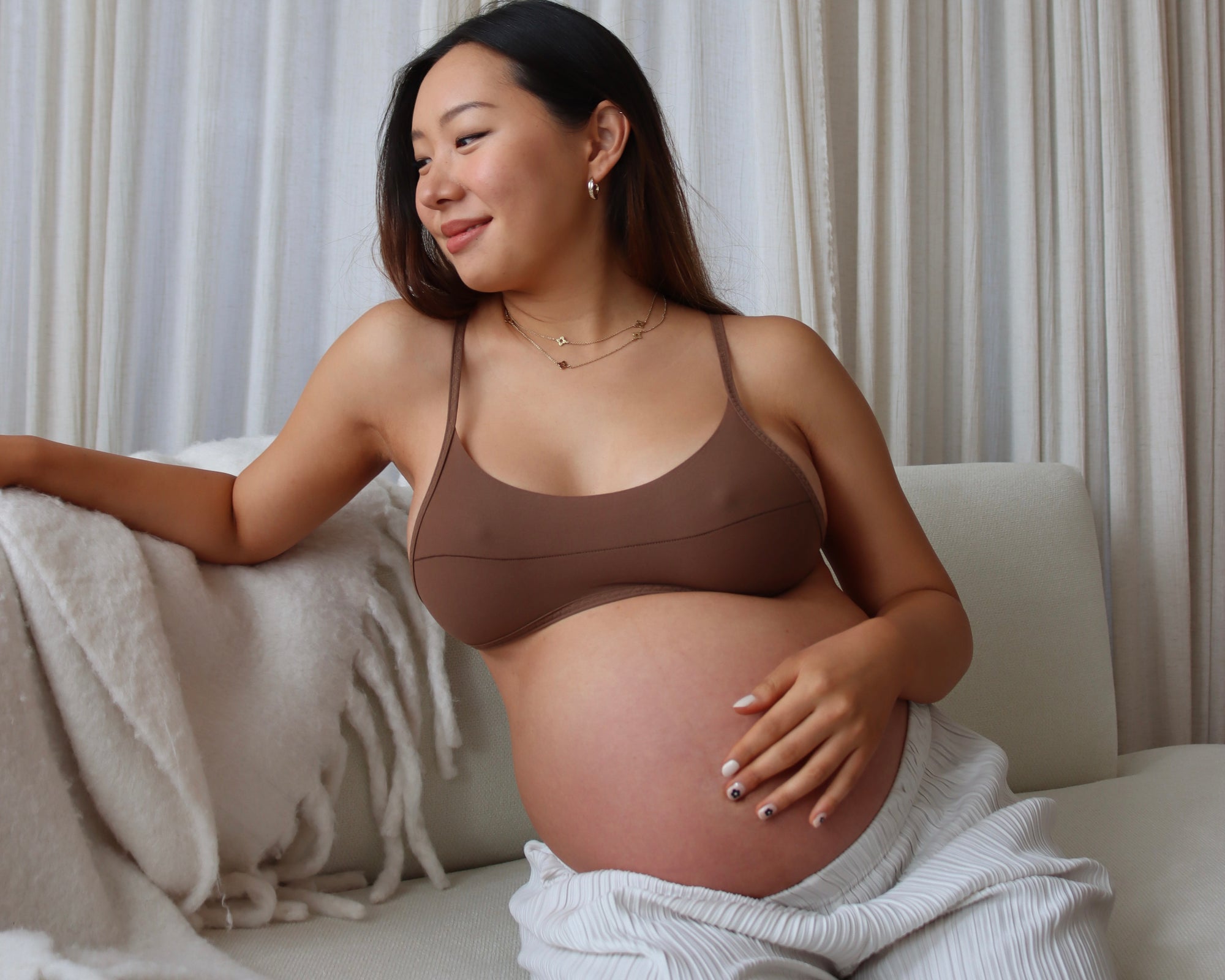 Pregnant woman sitting on a couch wearing the Scoop System in Brownz