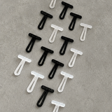 Twelve small plastic T-shaped toggles arranged in a loose diagonal pattern on a textured gray surface. The image is of 8 black pieces and 8 translucent white pieces.