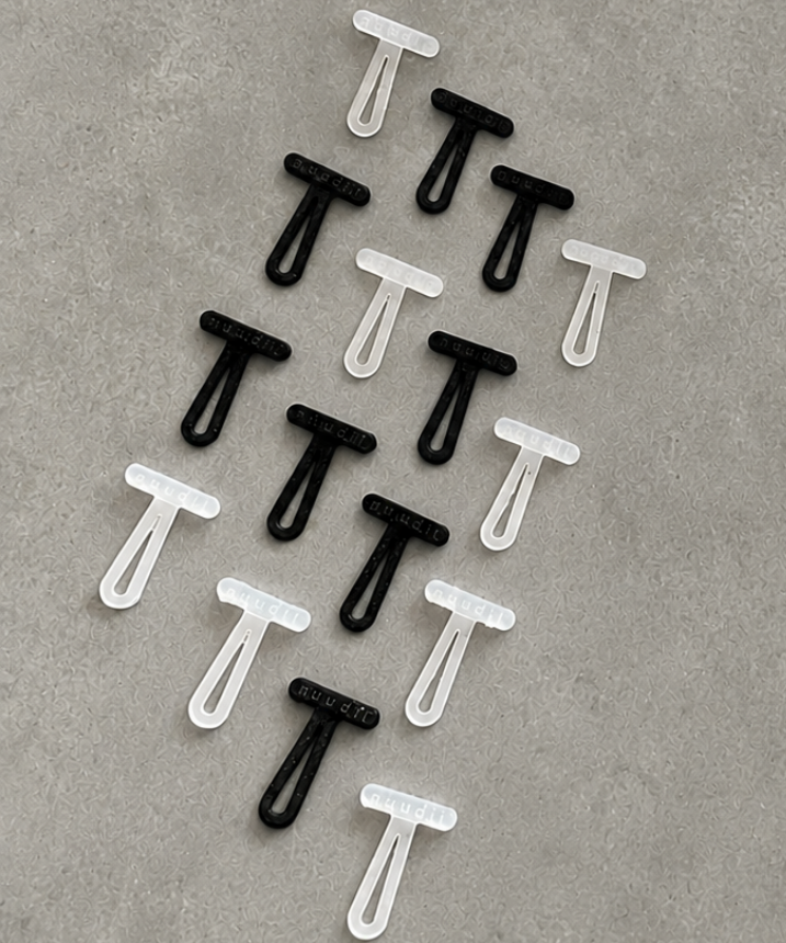 Twelve small plastic T-shaped toggles arranged in a loose diagonal pattern on a textured gray surface. The image is of 8 black pieces and 8 translucent white pieces.