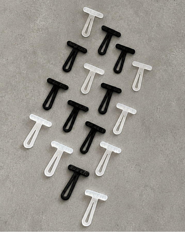 Twelve small plastic T-shaped toggles arranged in a loose diagonal pattern on a textured gray surface. The image is of 8 black pieces and 8 translucent white pieces.