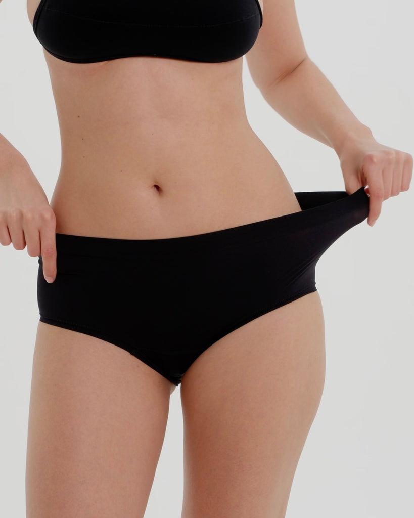 Person wearing black high-waisted underwear on a light gray background