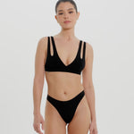 A woman wearing black thong underwear designed with a mid-rise cut.