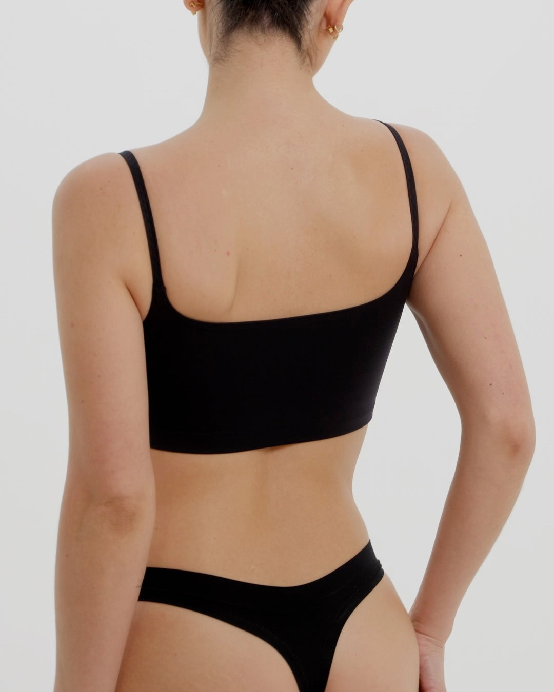 Person wearing a black bra and underwear on a plain background