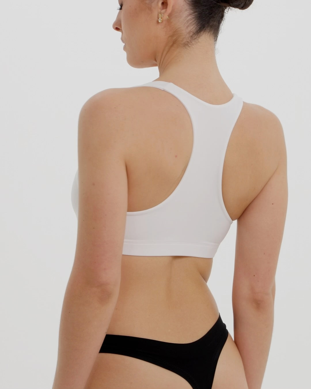 Woman wearing a white racerback on a plain background