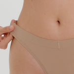 Woman wearing a beige thong against a plain background