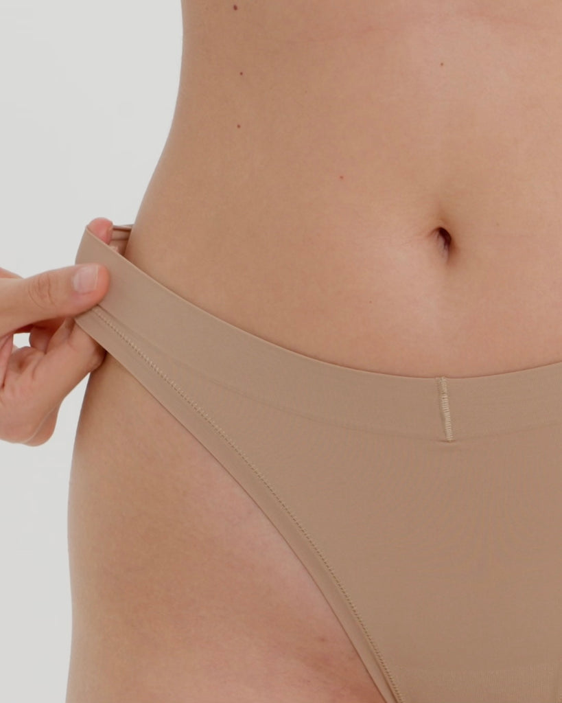 Woman wearing a beige thong against a plain background