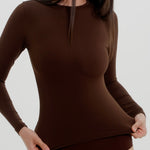 Woman wearing a brown long-sleeve against a plain background