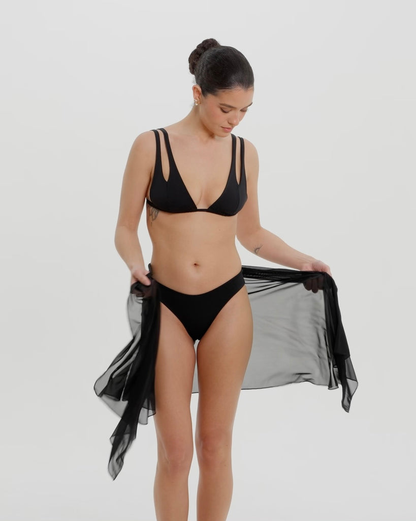 Black bikini with a tied sarong on a neutral background