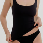 Woman wearing a black tank top and underwear on a gray background