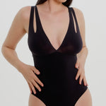 Woman wearing a black bodysuit against a plain background