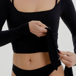 Woman wearing a black wrap top and black thong on a plain background